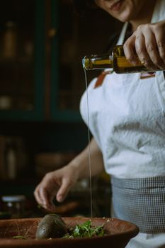 A chef skillfully pours olive oil on a fresh salad in a rustic kitchen setting.