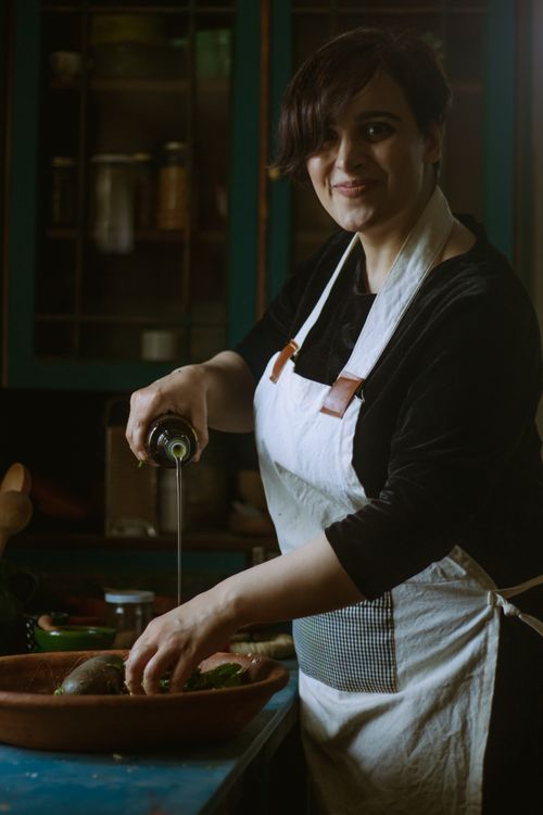 Free Woman in a cozy kitchen pouring olive oil onto vegetables while smiling. Stock Photo