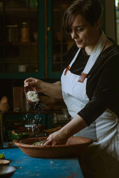 Free A woman in an apron prepares a meal, adding fresh ingredients to a bowl. Stock Photo