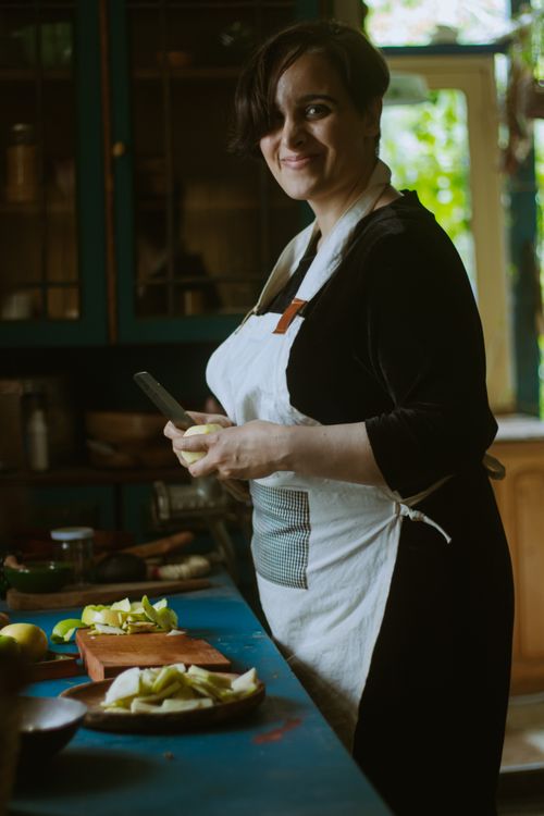 Free A woman in an apron slices fruit in a warmly lit kitchen, creating a homely atmosphere. Stock Photo