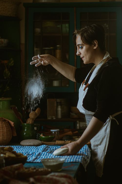 Free Woman sprinkling flour on dough in a cozy kitchen. Rustic ambiance with a focus on homemade cooking. Stock Photo