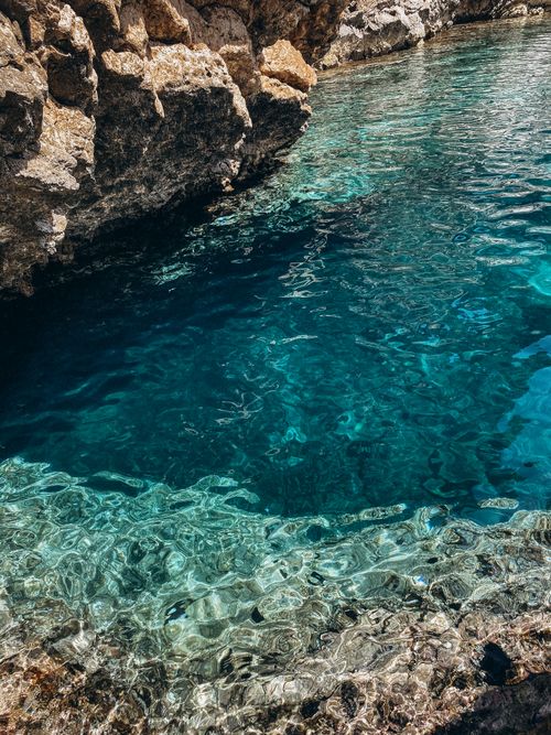 Free Stunning view of clear blue water along a rugged rocky coastline, perfect for travel and nature enthusiasts. Stock Photo