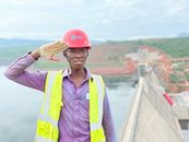 Woman in Yellow Vest and Red Cap Standing on Bridge