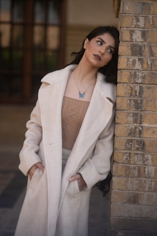 A Woman in White Coat Standing Beside Brick Wall