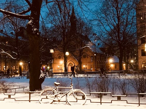 夜間のフェンス近くの雪に覆われた自転車