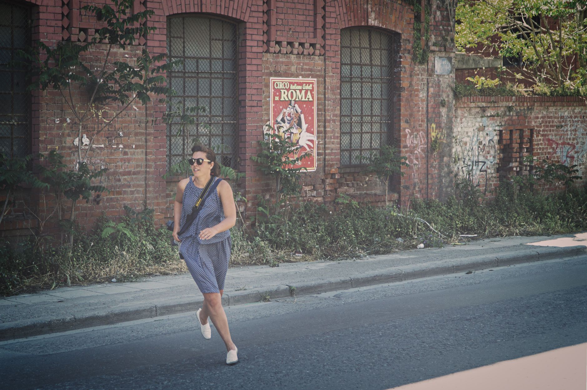 Young woman in summer dress jogging by an old brick building with graffiti and poster.