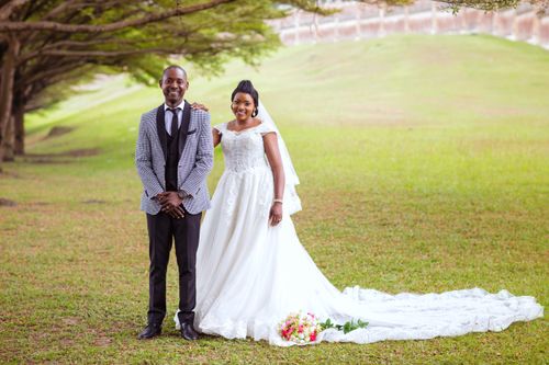 Free Happy newlyweds posing in elegant attire in a verdant field. Stock Photo