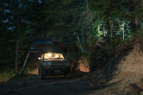 Free SUV parked with rooftop tent in a dimly lit forest campsite at night. Stock Photo