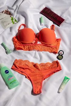 Bright orange lingerie and cosmetics laid out on a white fabric backdrop, perfect for beauty and fashion themes.