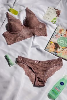 Stylish brown lace lingerie set on white fabric, accompanied by beauty products and magazines.