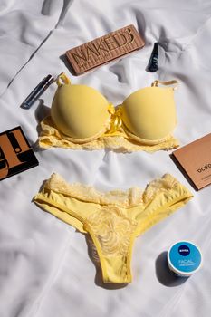 Flat lay of yellow lingerie set with beauty products on a white background.