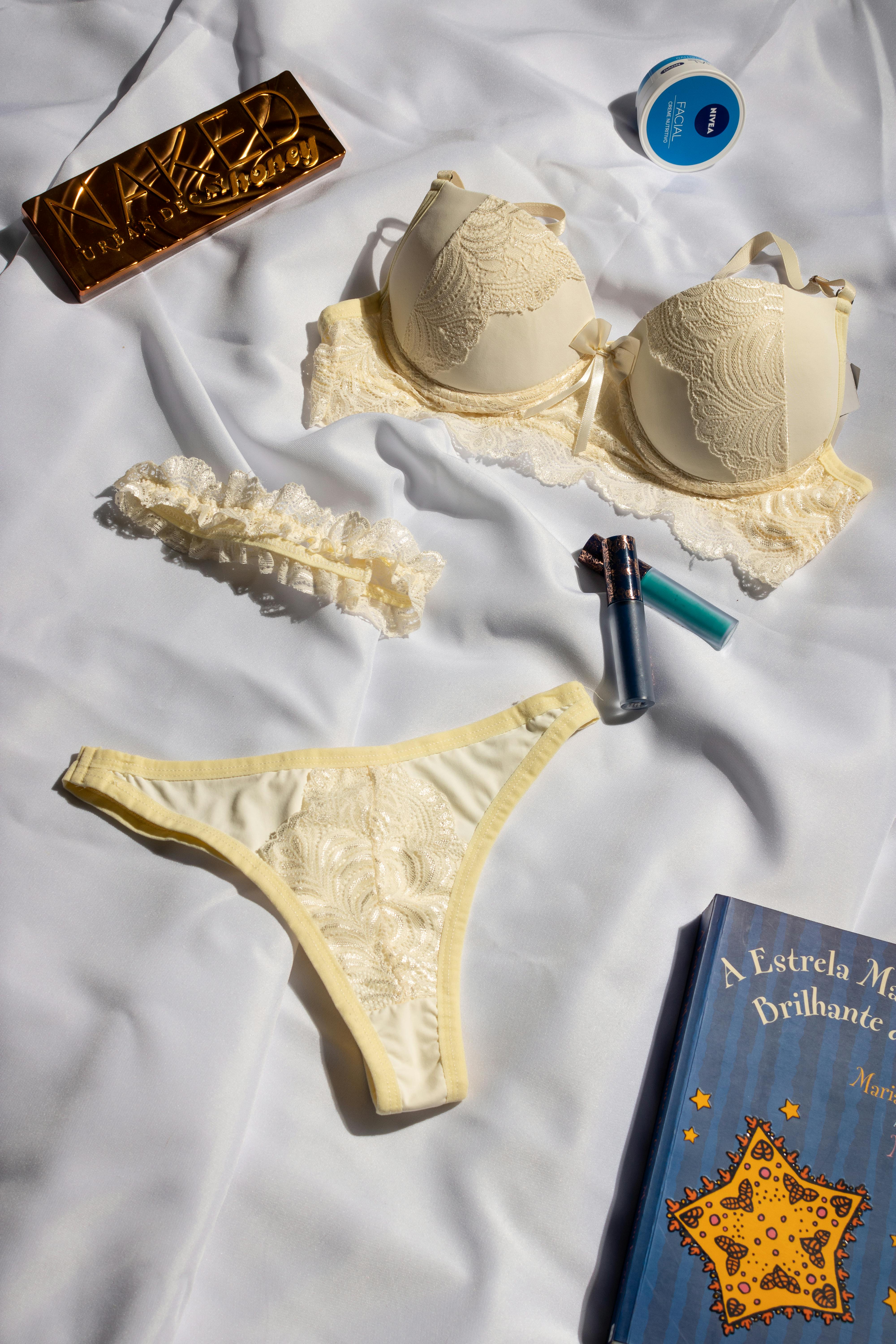 A stylish display of cream lingerie, cosmetics, and a book on a silk background.