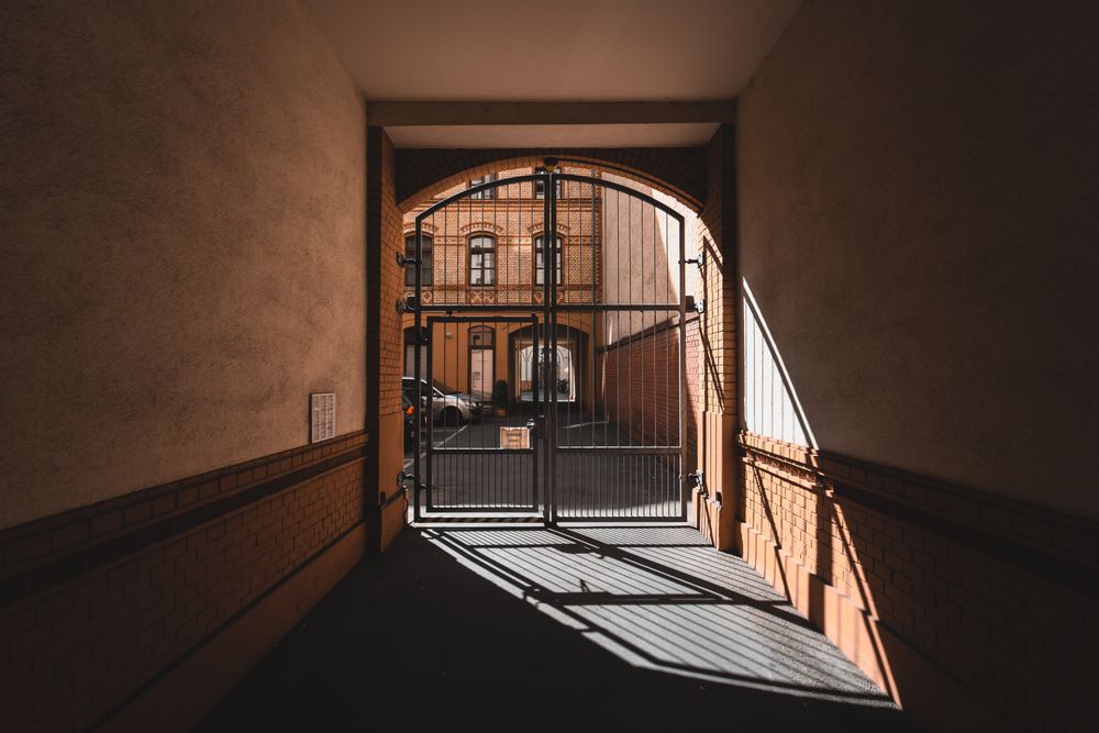 Ornate metal gate with architectural details and a sunlit passage