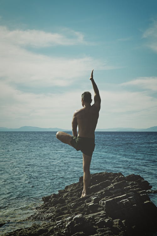 Free Topless Man Standing on Rock Formation Using Right Leg Only Stock Photo