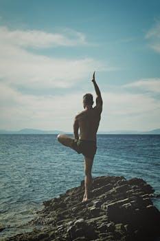 Back view of a man practicing yoga on a rocky seashore. Embracing peace, meditation, and nature.