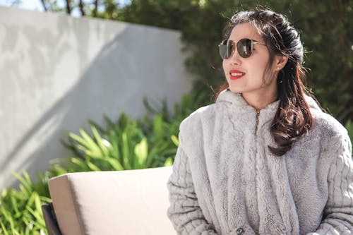 Mujer Vestida Con Abrigo De Piel Gris Y Gafas De Sol Sentado Cerca De Plantas De Hojas Verdes