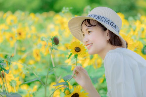 Girl in White Sun Hat Smelling Yellow Flower