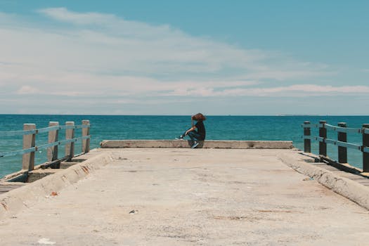 A young woman sitting alone on a seaside dock under a clear blue sky.