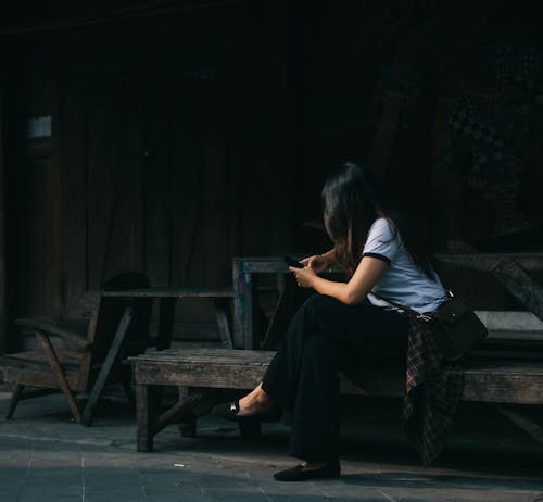 Женщина в белой рубашке с круглым вырезом сидит на коричневой деревянной скамье