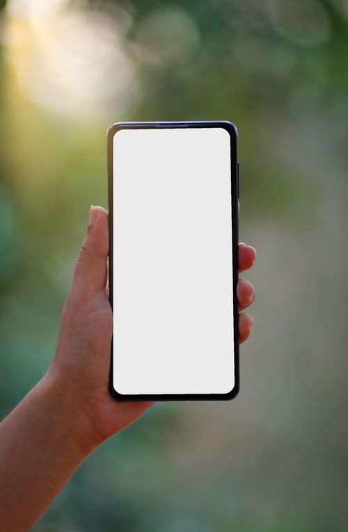Free Hand holding a smartphone with a blank screen outdoors, ideal for mockup use. Stock Photo