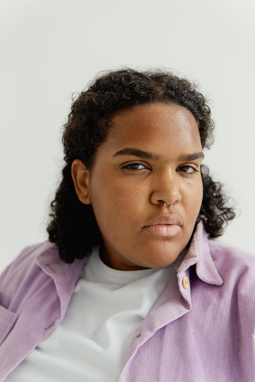 Free Portrait of a confident young woman with curly hair and natural beauty, wearing a casual lavender shirt. Stock Photo