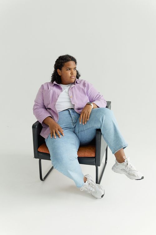 Free Woman in purple shirt and denim sitting on chair, looking thoughtful. Stock Photo