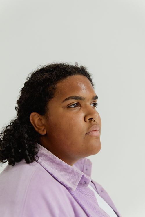 Free Close-up portrait of a thoughtful woman looking sideways in a studio setting, wearing a purple shirt. Stock Photo