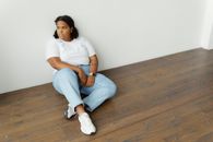 Woman in White Shirt Sitting on Wooden Floor while Leaning on White Wall