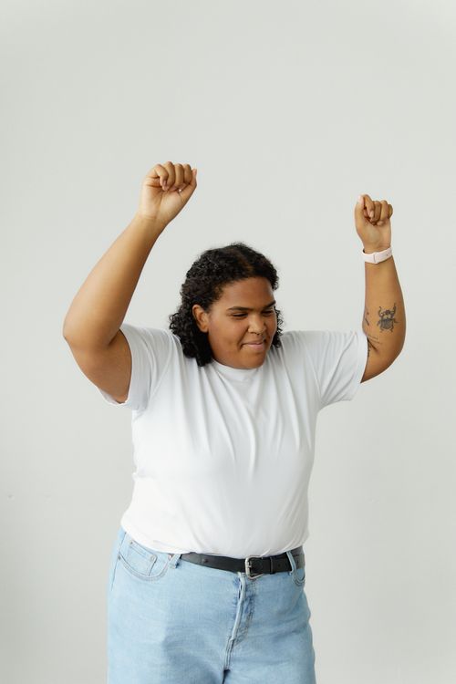 Free Happy plus-size woman in casual outfit expressing joy with raised hands against a white backdrop. Stock Photo