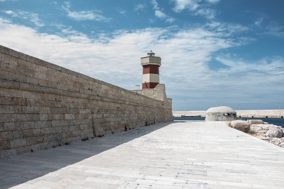 A picturesque lighthouse by the seashore with a stone wall and blue sky, perfect for travel or architecture themes.