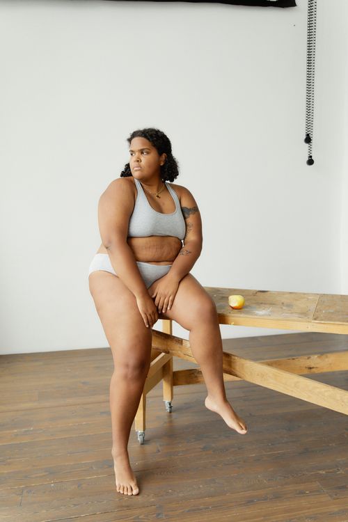 Free A confident black woman poses in a bikini while sitting on a wooden table with minimal decor. Stock Photo