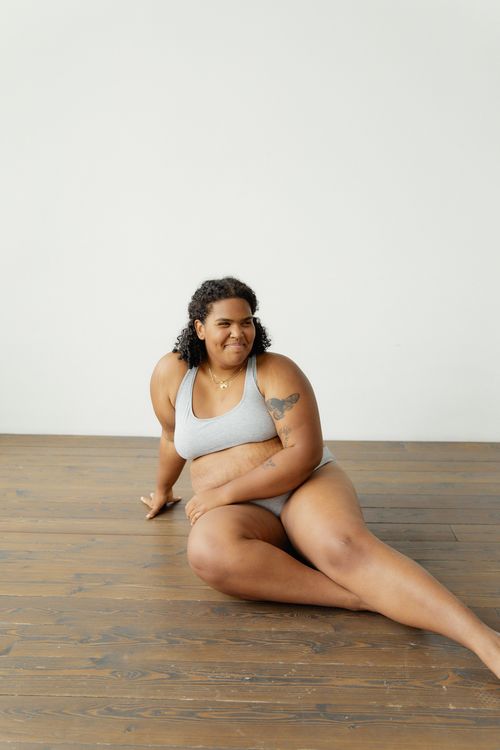 Free A confident plus size African American woman in grey lingerie poses on a wooden floor, embodying self-love and positivity. Stock Photo
