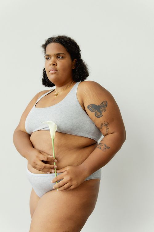 Free Body positive plus-size woman with tattoos holding a white flower in a minimalist setting. Stock Photo