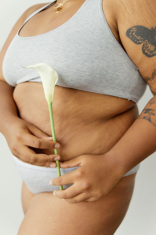 Free Up-close image of a tattooed woman embracing body positivity, holding a white lily. Stock Photo