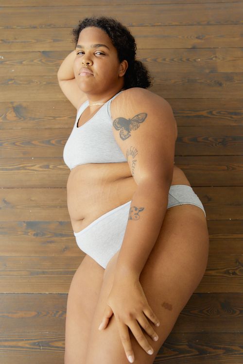 Free Confident plus size woman in lingerie posing on a wooden floor, promoting body positivity. Stock Photo
