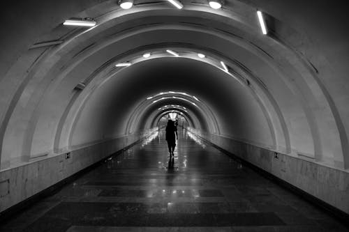 Grayscale Photo of Person Walking in a Tunnel