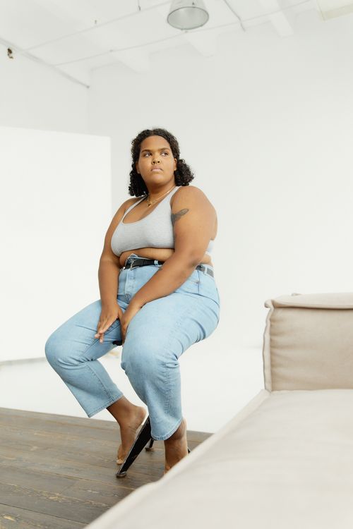 Free Portrait of a confident plus-size woman sitting indoors in a modern, minimalist setting, wearing casual attire. Stock Photo