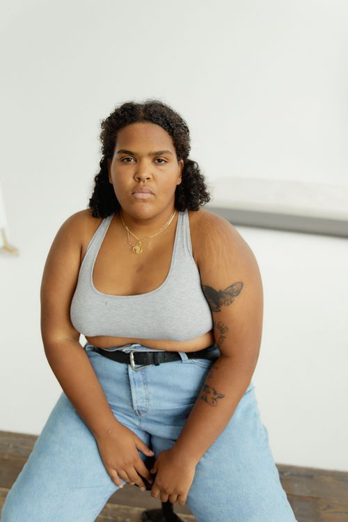 Free Portrait of a confident plus-size black woman sitting indoors, showcasing body positivity and casual fashion. Stock Photo