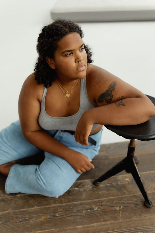 Free Confident plus-size woman in casual outfit leaning on stool, embracing body positivity. Stock Photo