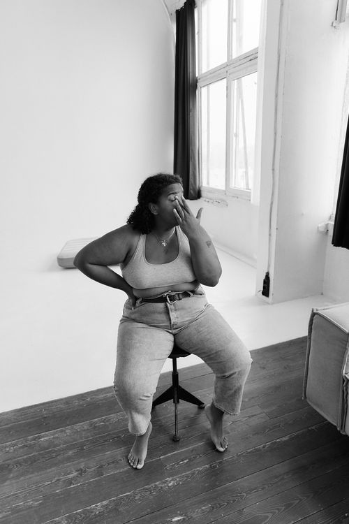 Free Black and white photo of a plus size woman sitting on a stool in a minimalist studio. Stock Photo