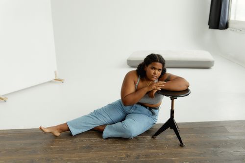 Free Plus size woman in denim jeans, bra top, leaning on a stool in a bright studio. Stock Photo