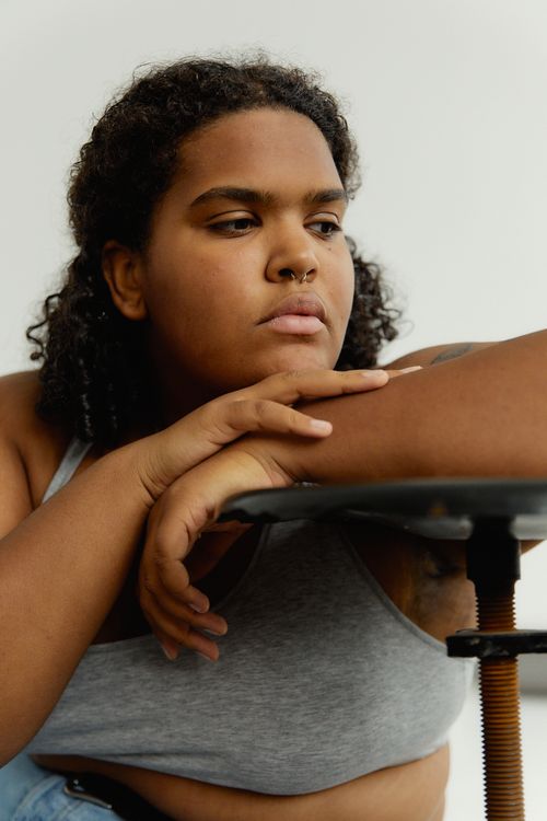 Free A contemplative young woman with curly hair leaning on a table indoors. Stock Photo