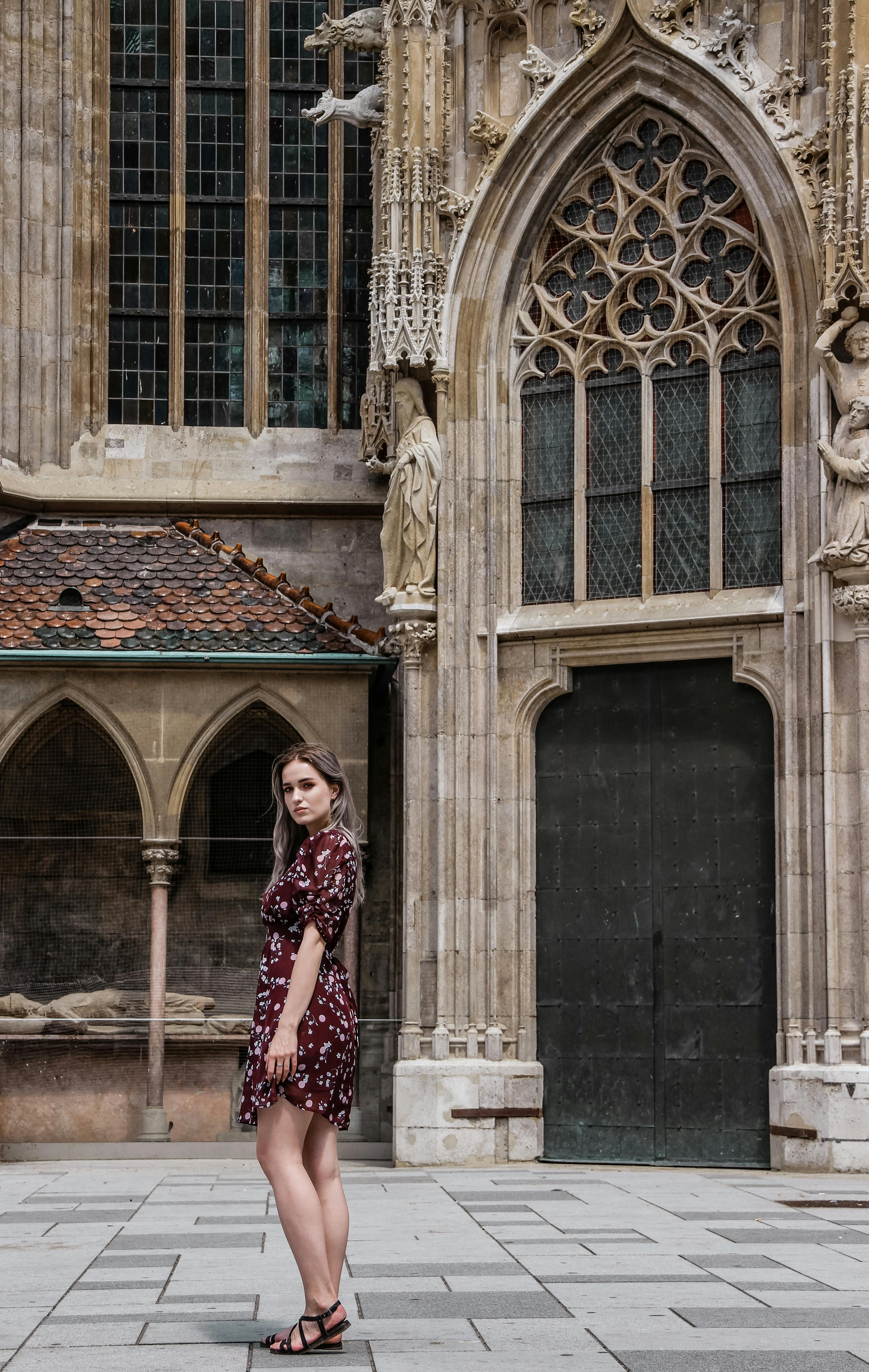 Woman in a floral dress posing by a gothic building, showcasing fashion against historical architecture.