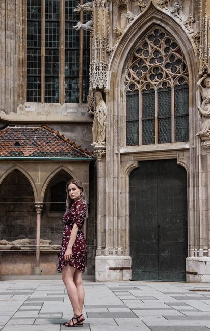 Woman in a floral dress posing by a gothic building, showcasing fashion against historical architecture.