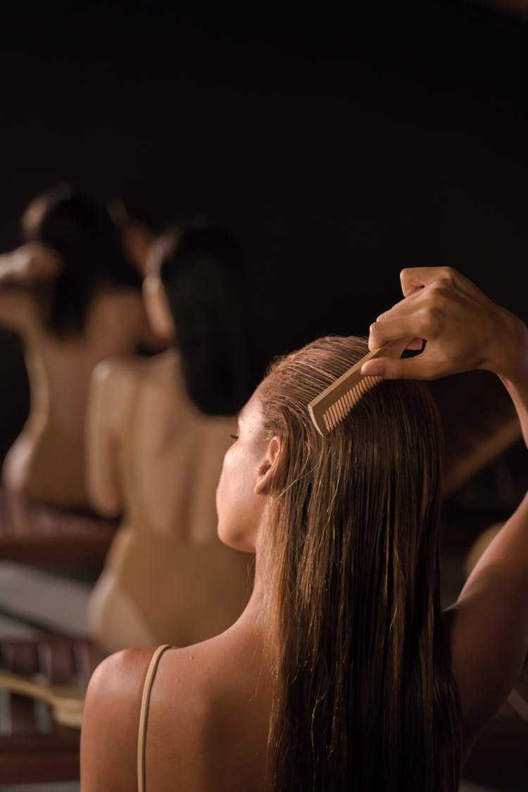 A Brunette Woman Brushing Her Hair Using A Wooden Comb 