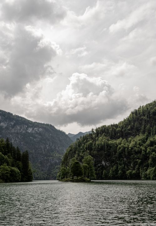 Free A serene mountain lake surrounded by lush greenery under a cloudy sky, offering a peaceful natural landscape. Stock Photo