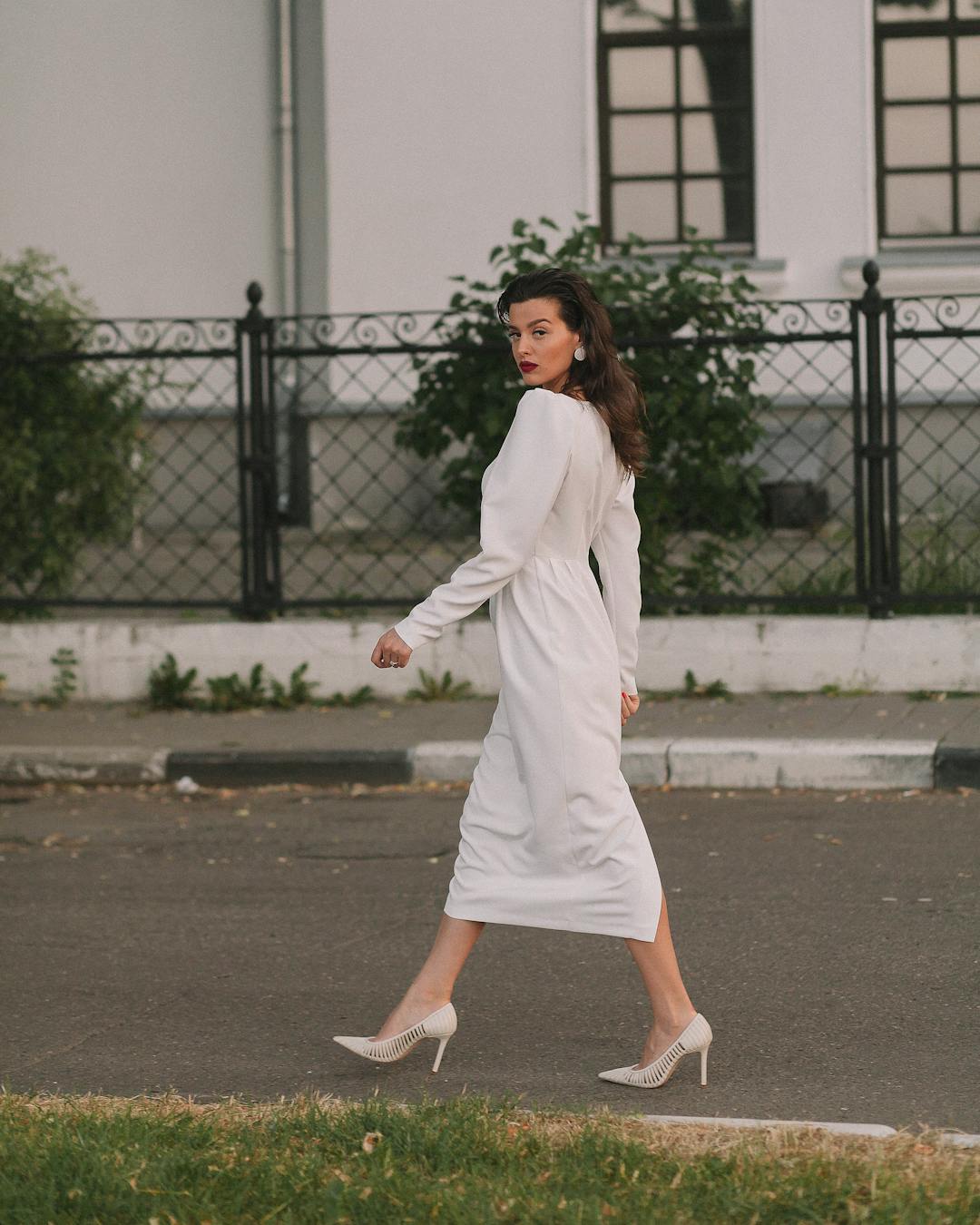 Stylish woman in white dress walking past a fence in Yaroslavl, Russia on a sunny day.