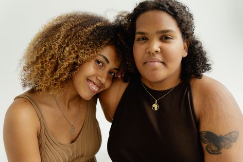 Free Two women with curly hair and necklaces smile warmly as they embrace, showcasing sisterhood and friendship. Stock Photo