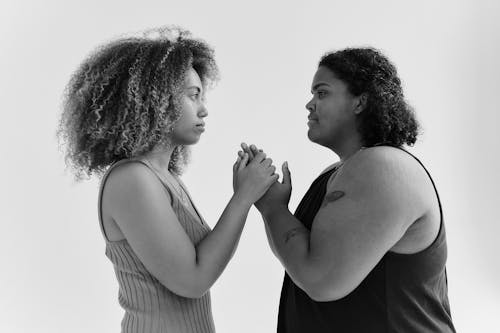 A Grayscale Photo of Women Holding Hands while Looking at Each Other
