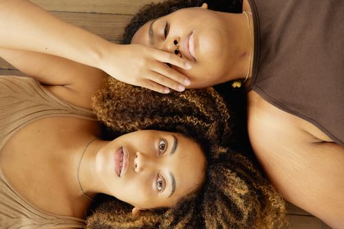 Free Two women with afro hair lying together on a wooden floor. Captured in warm tones. Stock Photo
